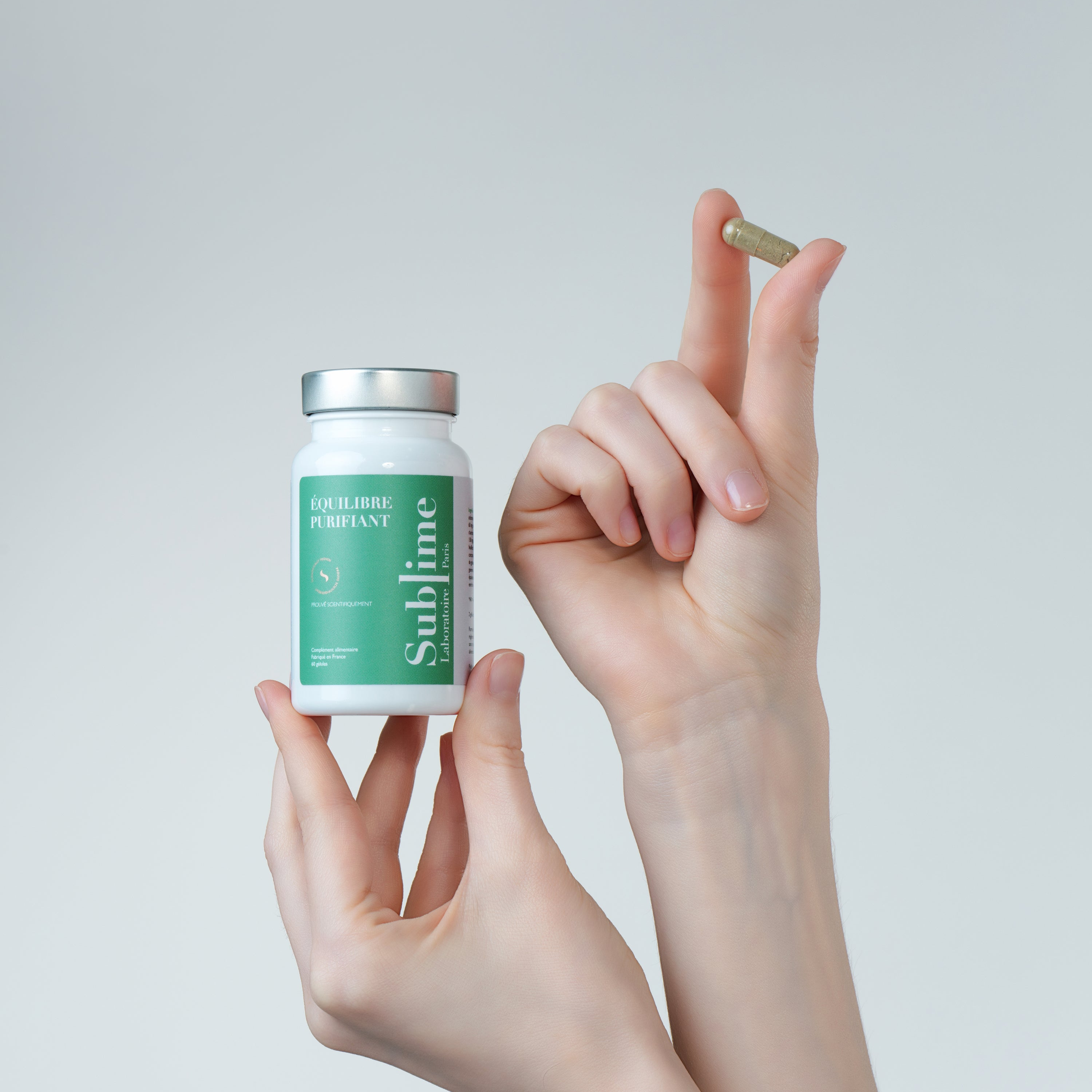 Hand holding Laboratoire Sublime Purifying Balance detox supplement bottle and capsule, French liver and skin detox formula, studio shot on light background.