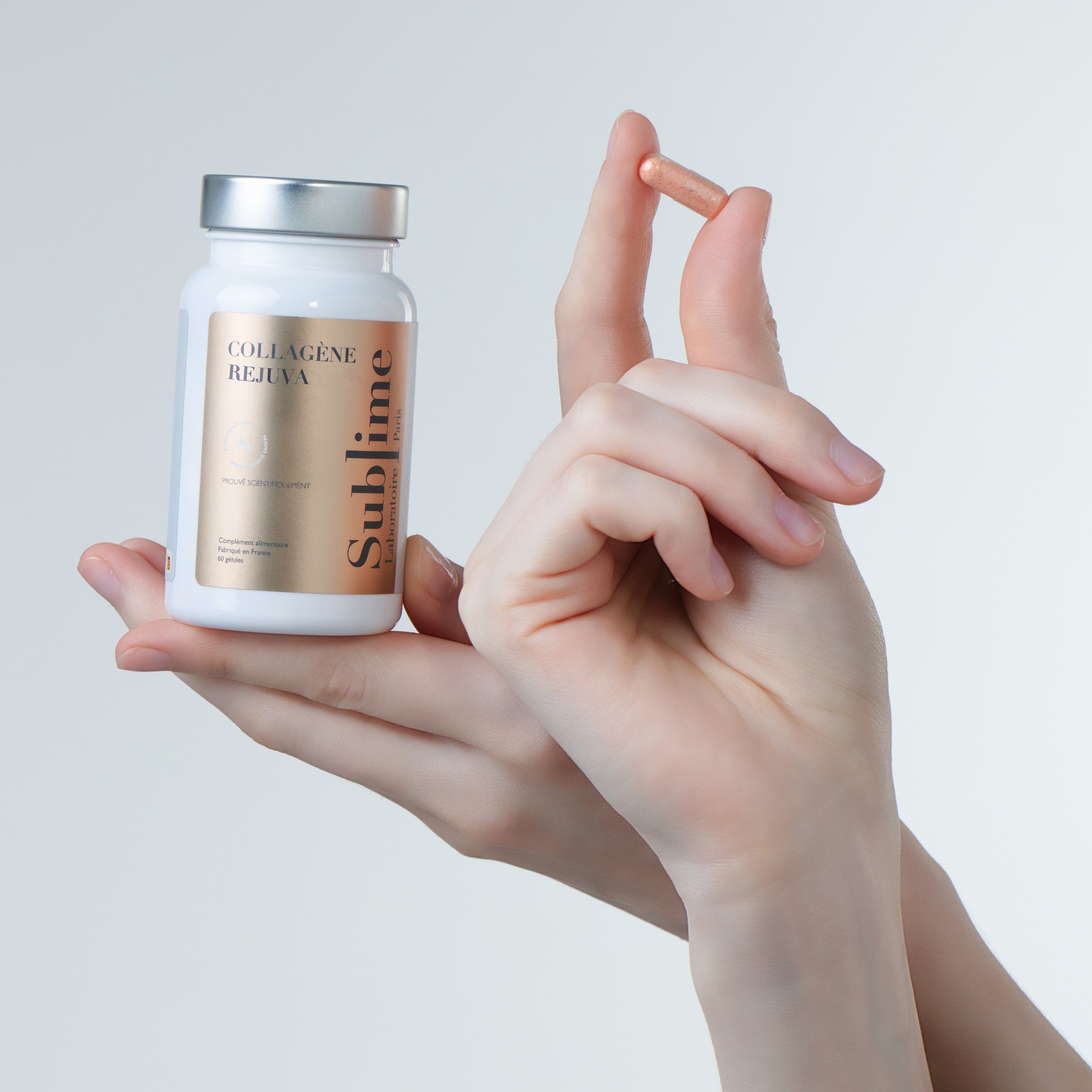 Hand holding Laboratoire Sublime Rejuva Collagen supplement bottle and capsule, French collagen beauty supplement for skin firmness, front view on gray background.