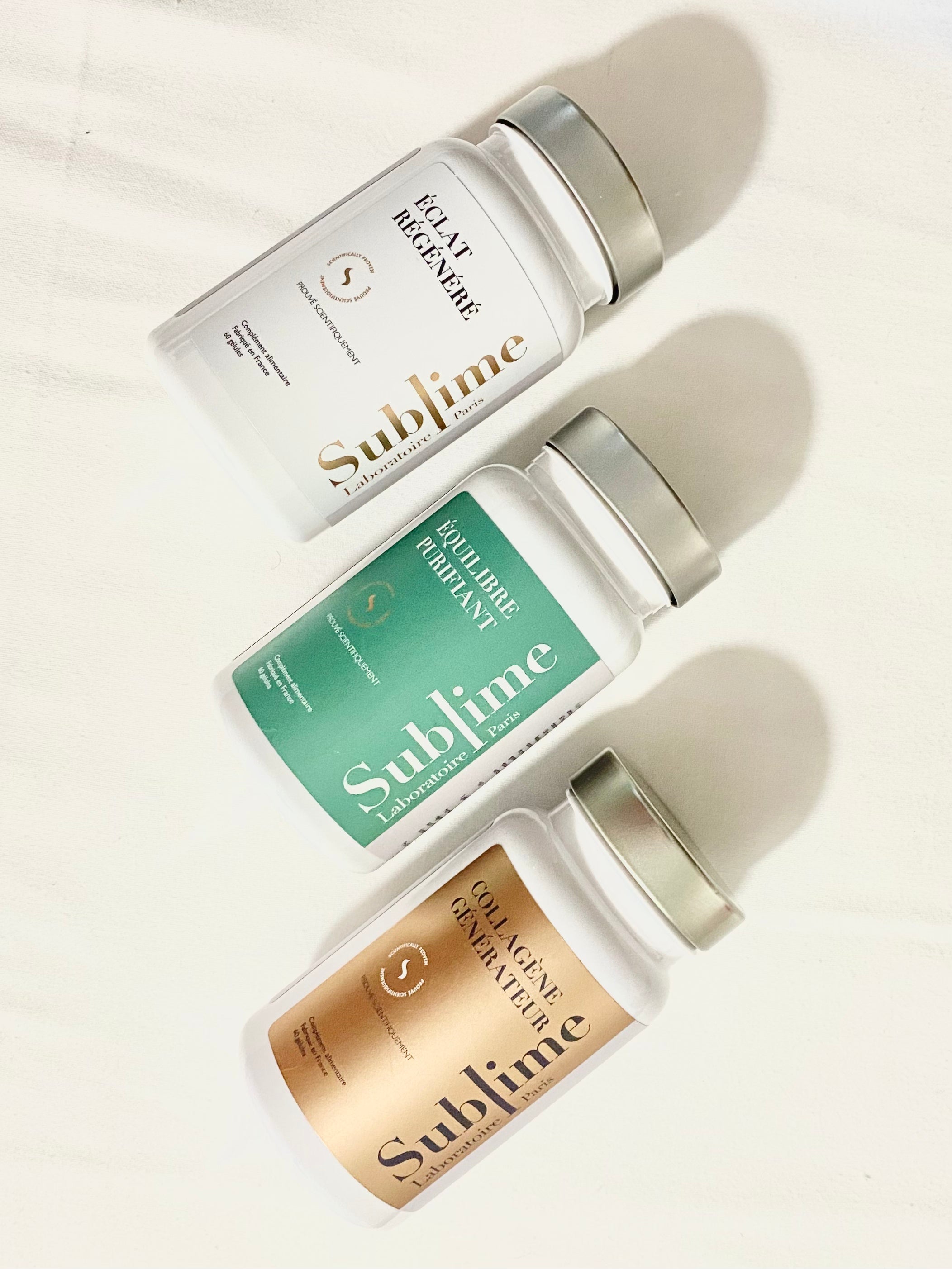 Three Laboratoire Sublime supplement bottles, French beauty & wellness collagen supplements, Rejuva Collagen, Regenerated Radiance, and Purifying Balance, flat lay on beige background