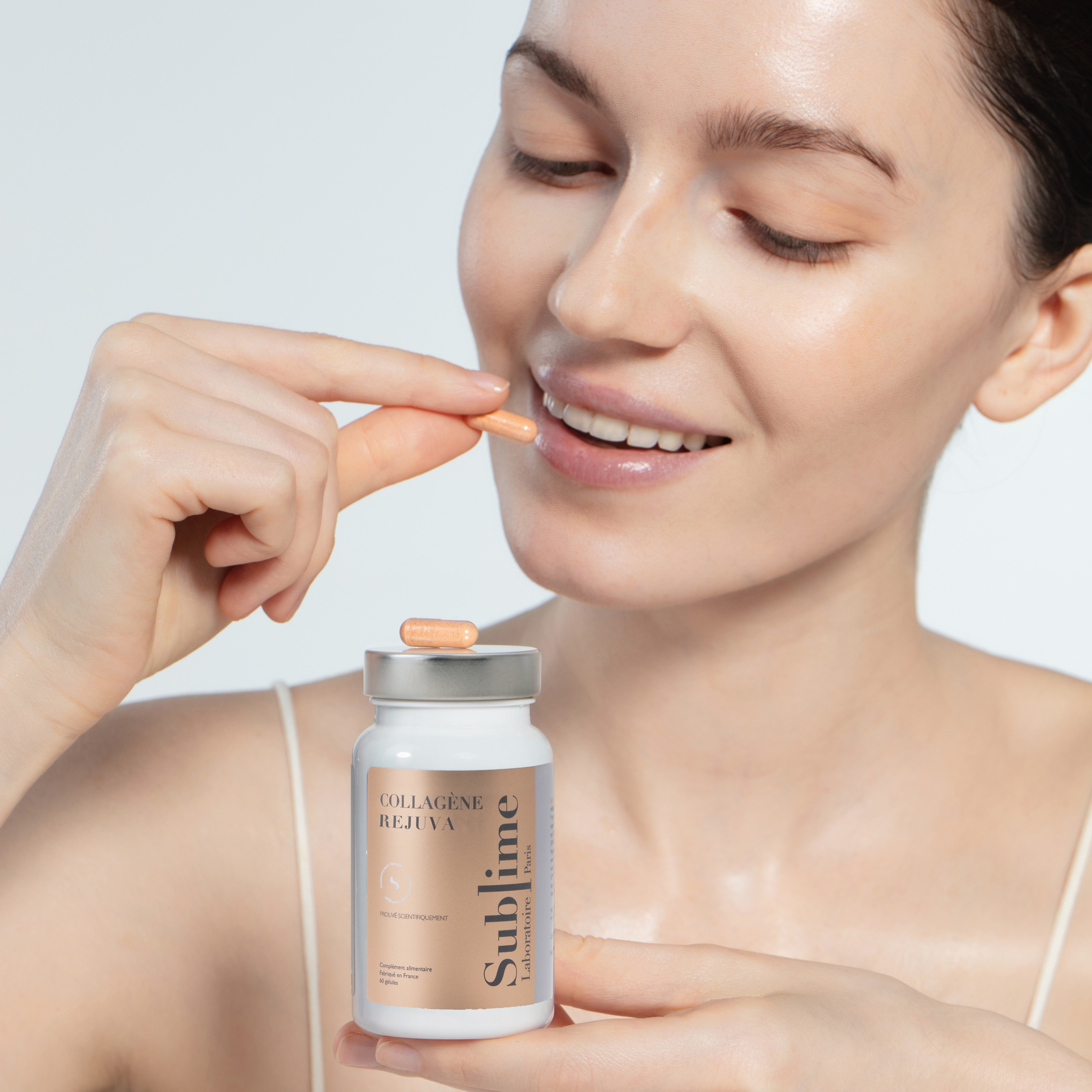 Woman holding Laboratoire Sublime Rejuva Collagen bottle and collagen capsule, French beauty supplement for skin glow, front portrait on white background.