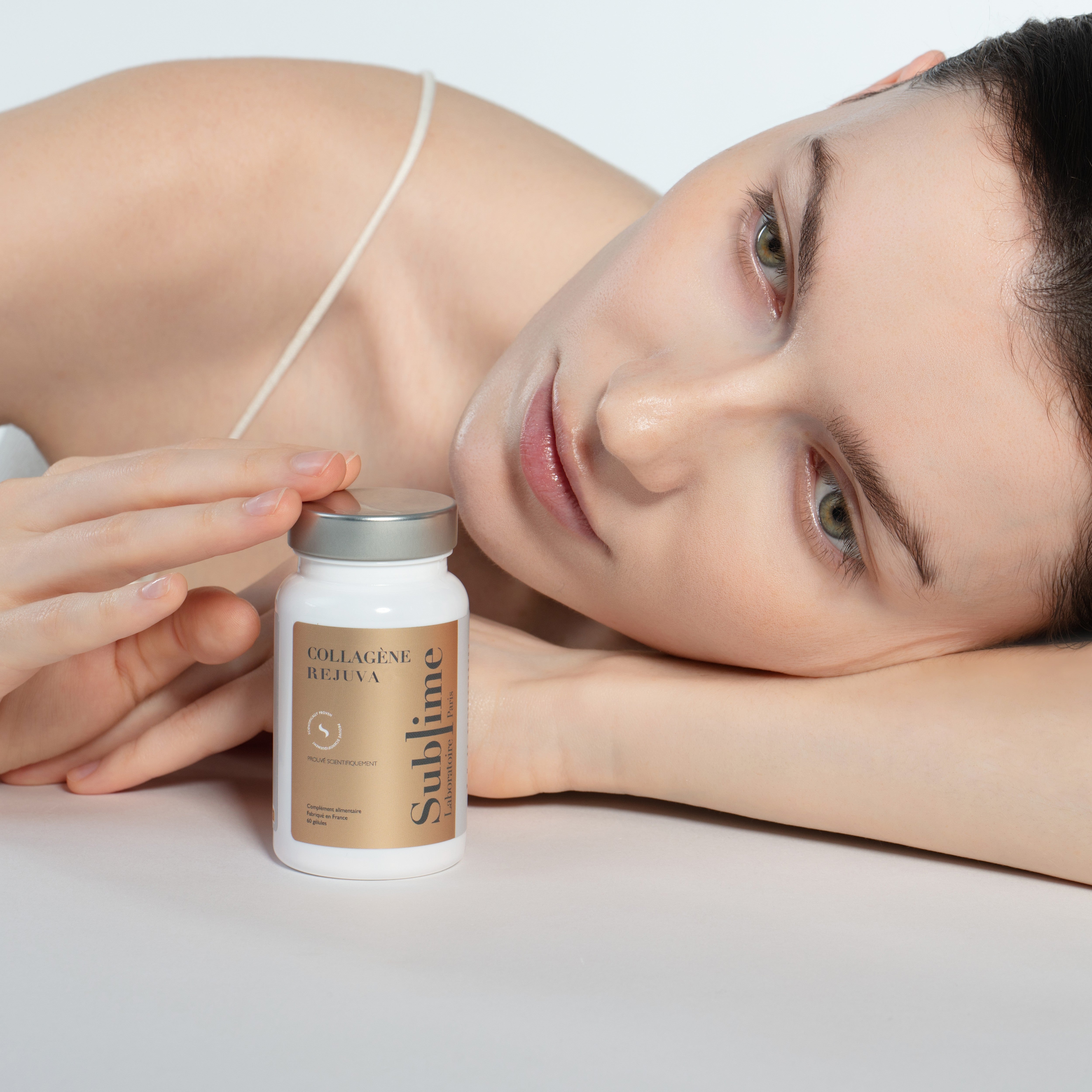 Woman holding a bottle of Collagène Rejuva by Laboratoire Sublime on a light background.